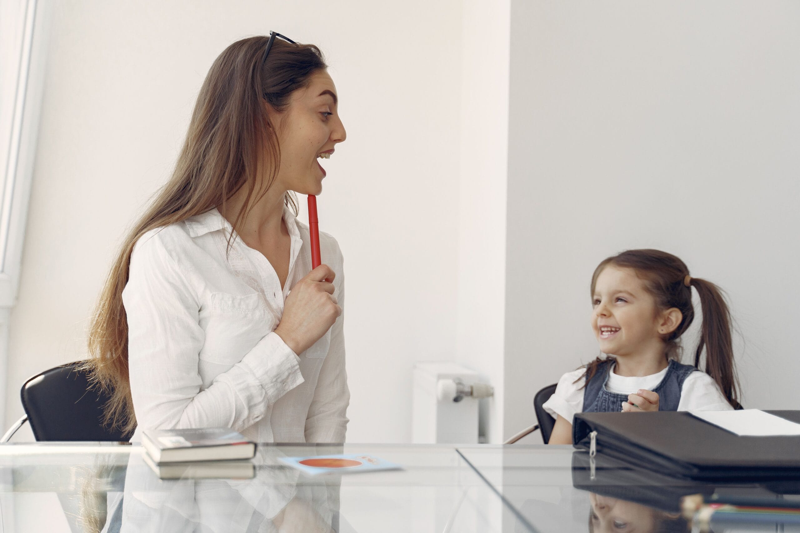 Un logopeda sonriendo a una niña de 5 años  para estimular el contacto visual y la sonrisa social.