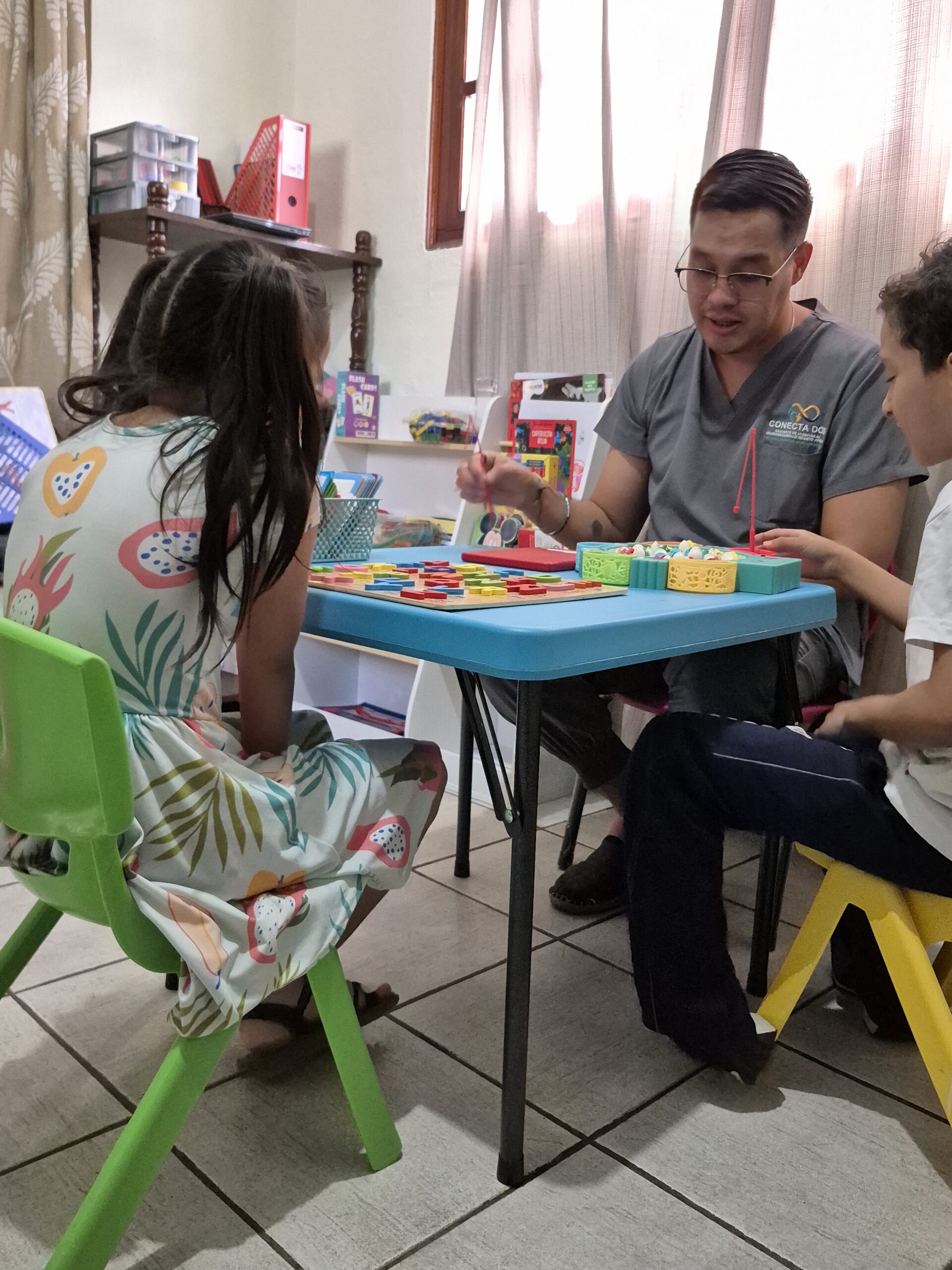 Mamá y su bebé de 18 meses sentados en una mesa de trabajo infantil, manipulando un juguete educativo en Centro Conecta - Dos.